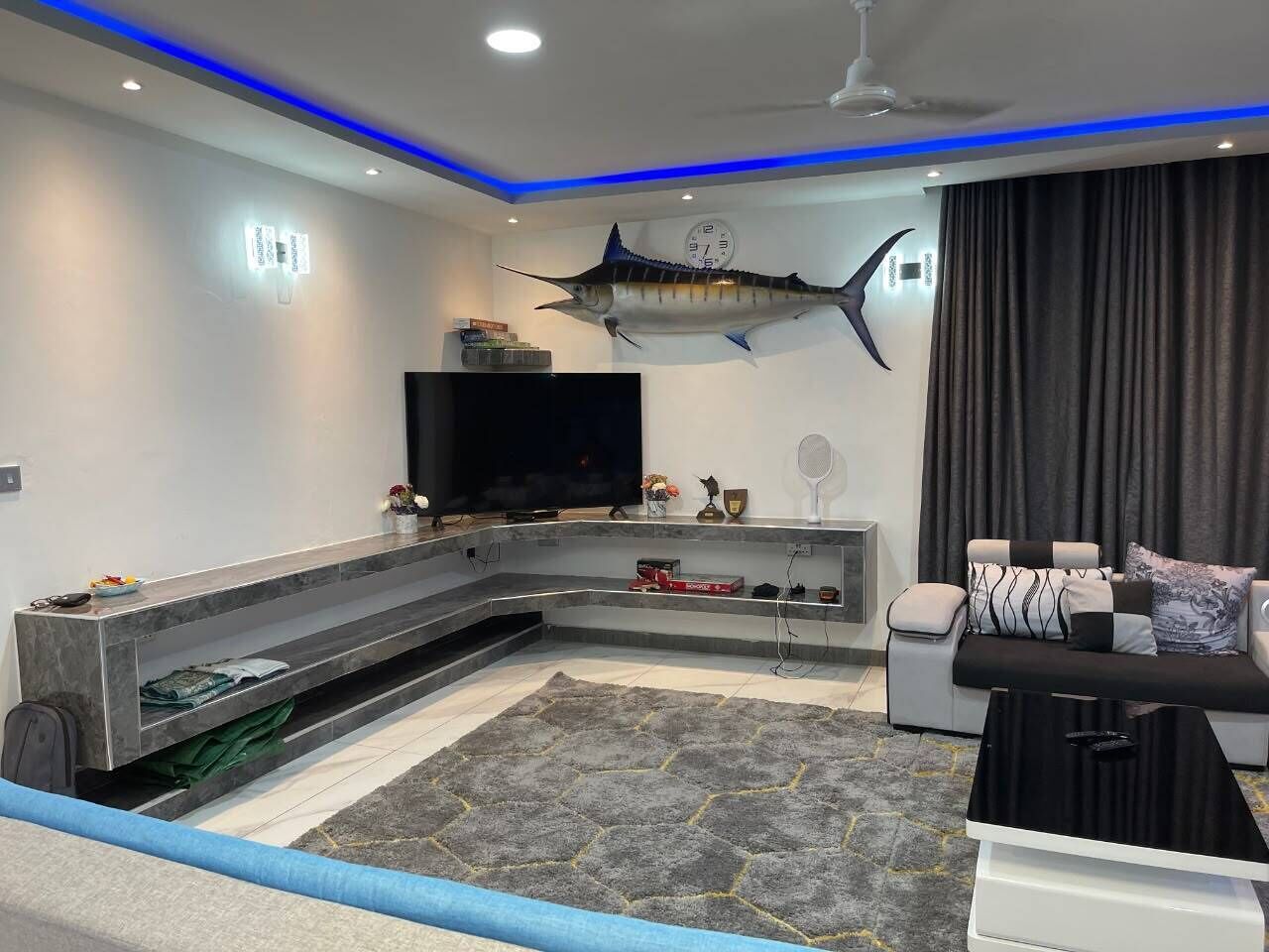 A modern living room with a large flat-screen TV, a mounted fish sculpture, a sofa, and a coffee table.
