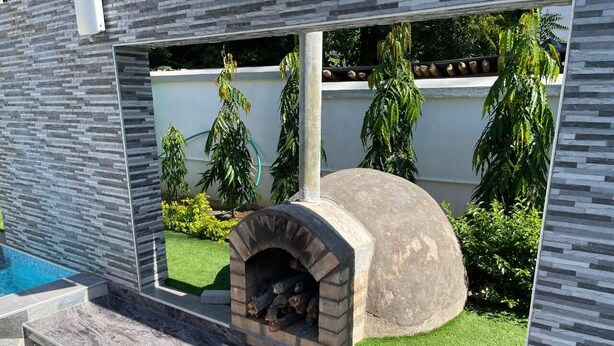 A stone-built outdoor fireplace with a stone bench in front, surrounded by a pool and greenery. - A Luxurious 5-Bedroom Kids friendly Private Villa in the Heart of Watamu. (Kilifi)