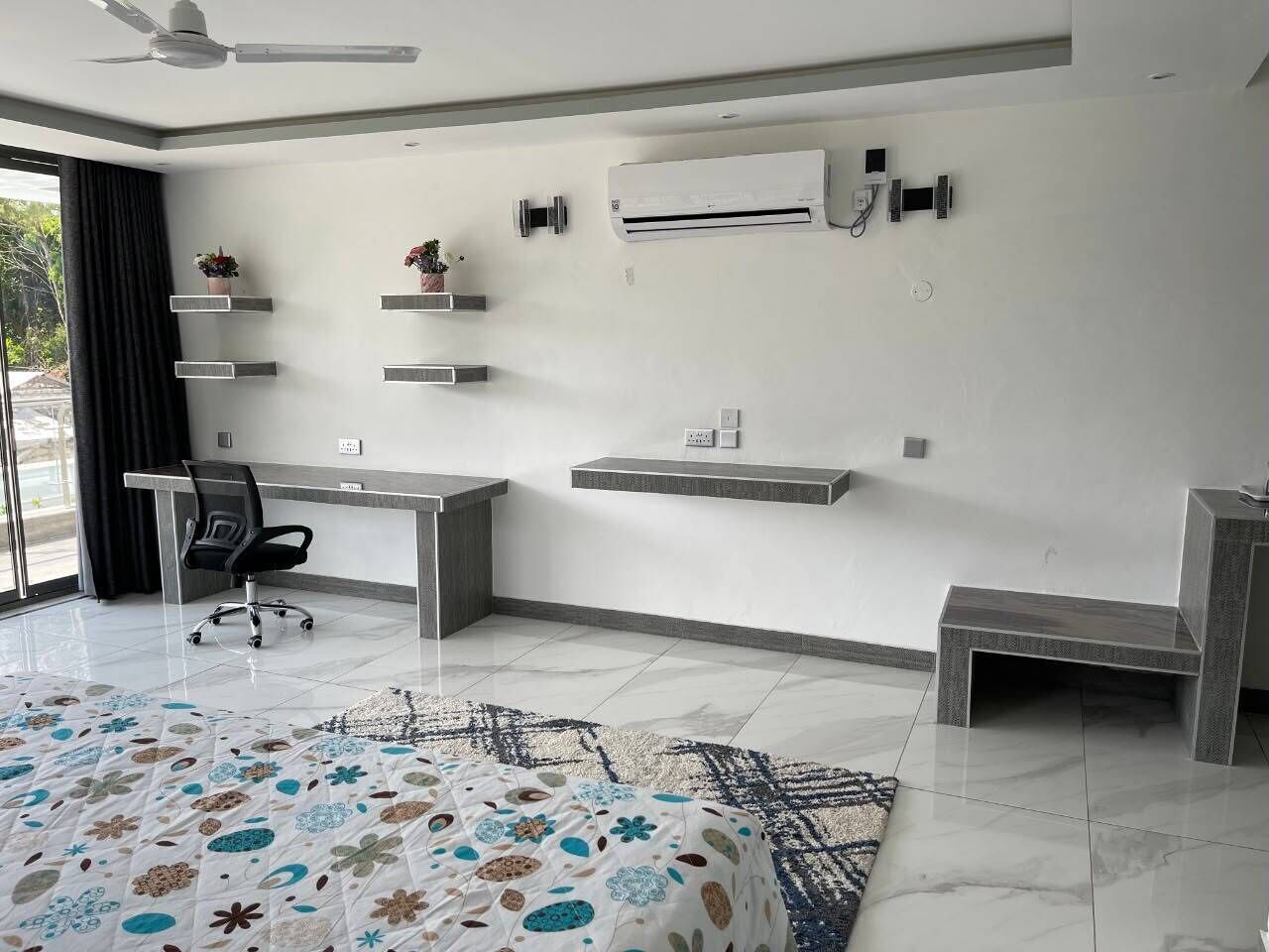 A modern room with a desk, chair, air conditioning unit, and decorative shelves.