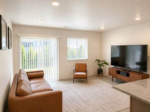 A living room with a sofa, a chair, a television, and a plant.