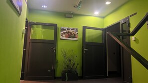 A hallway with green walls, two doors, a potted plant, and a sign above the doors.