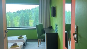 A hotel room with a bed, a desk, a chair, a TV, and a window with a view of trees.