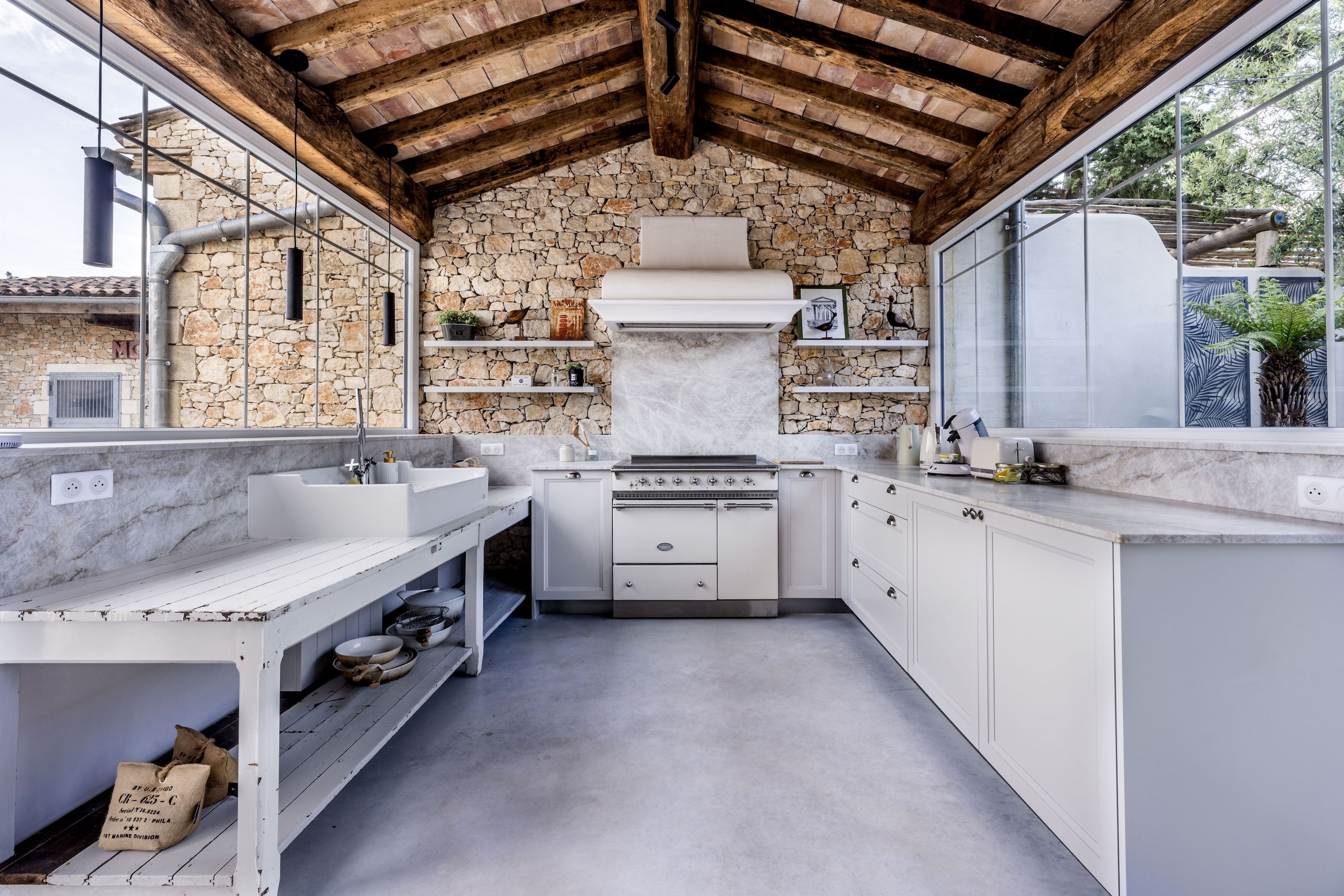 Une cuisine avec un mur en pierre, des meubles blancs et une grande fenêtre.
