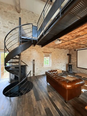 Una escalera de caracol, un sofá de cuero y un interior con pared de piedra.