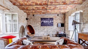 Une pièce avec un mur en briques, un grand canapé en cuir, un fauteuil suspendu et une table en bois.