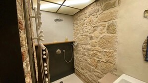 Une salle de bain avec une douche, un lavabo et un mur en pierre.