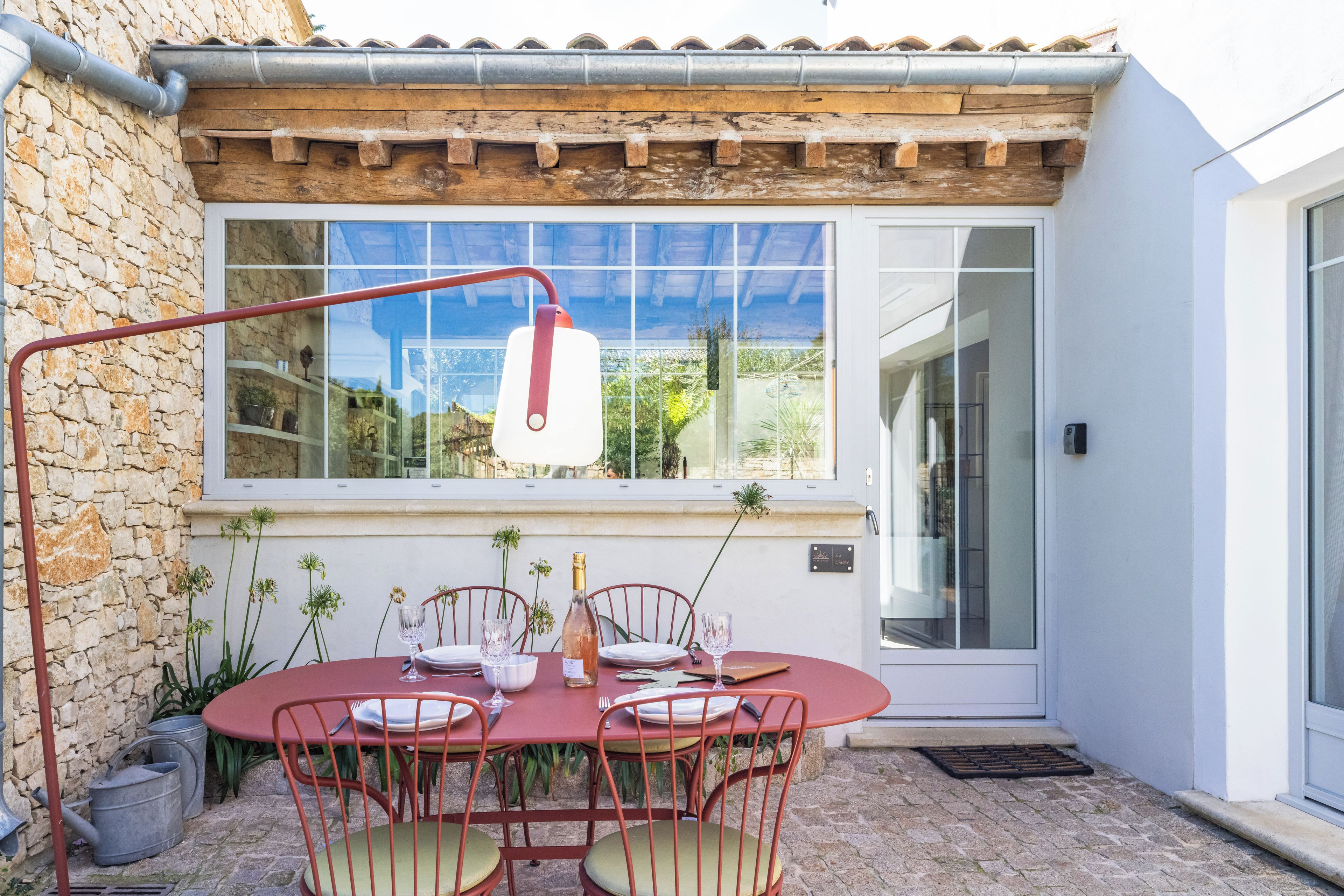An outdoor dining area with a stone wall, a wooden pergola, and a glass door leading to a modern interior.