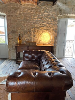A brown leather sofa in a room with stone walls and wooden flooring.