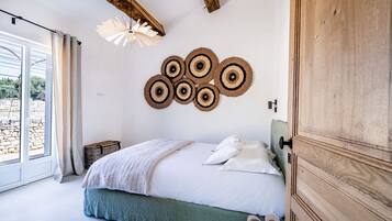 A bedroom with a bed, pillows, a wooden wardrobe, a wall-mounted light fixture, and a view through a window.