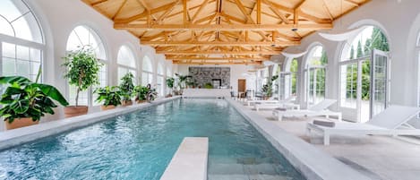 An indoor swimming pool with a wooden ceiling and arched windows.