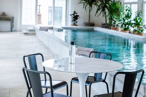 An indoor swimming pool area with a round table and chairs, a bottle, and glasses.