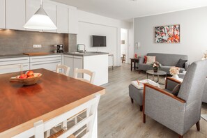Eine moderne Küche mit weißen Schränken, einem Holzespeisetisch und einem grauen Sofa im Wohnbereich.