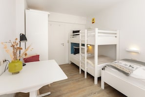 Ein Schlafraum mit Etagenbett, Schreibtisch, Lampe und einer Vase mit Trockenblumen.