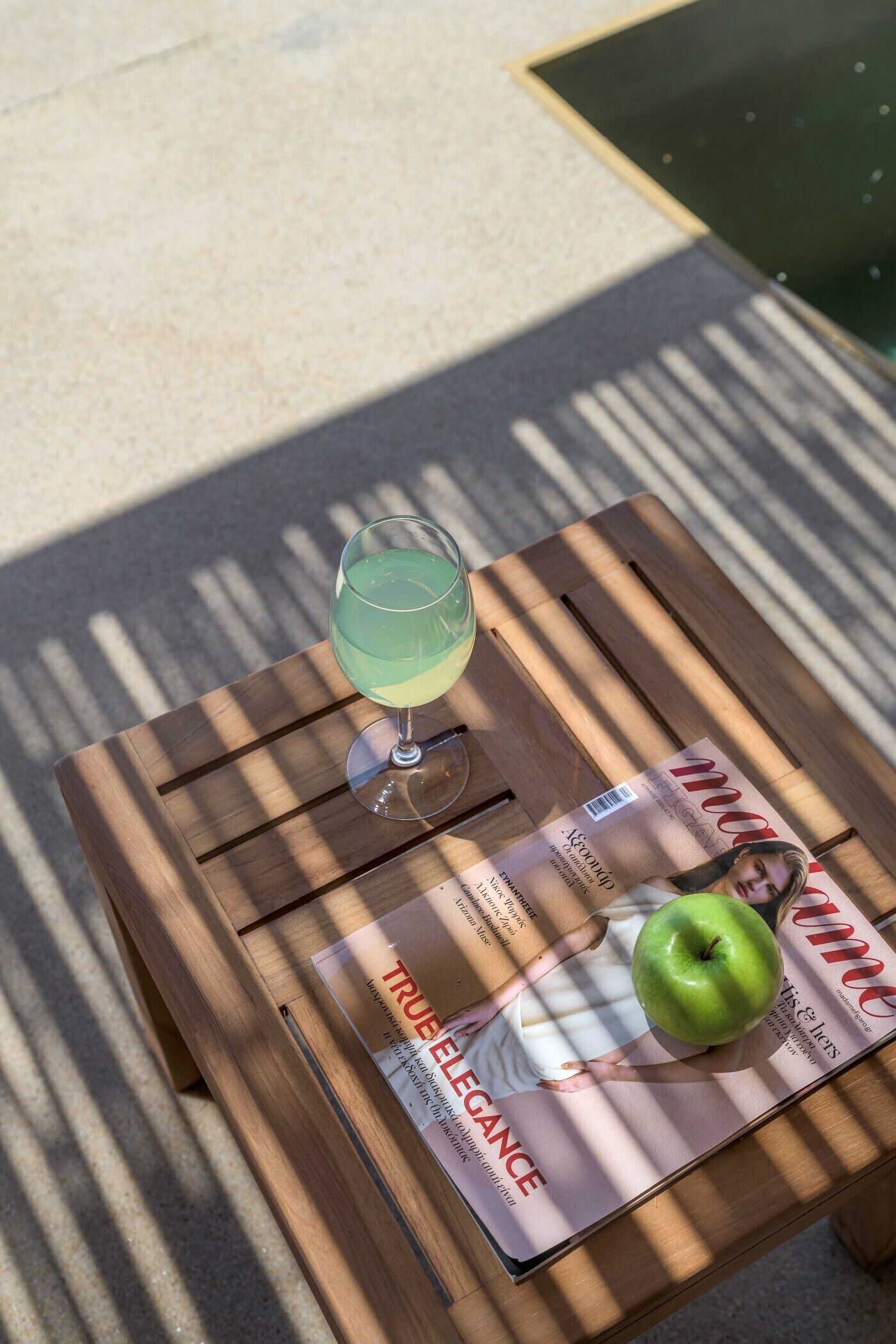 A wooden table with a magazine, a glass of drink, and an apple.