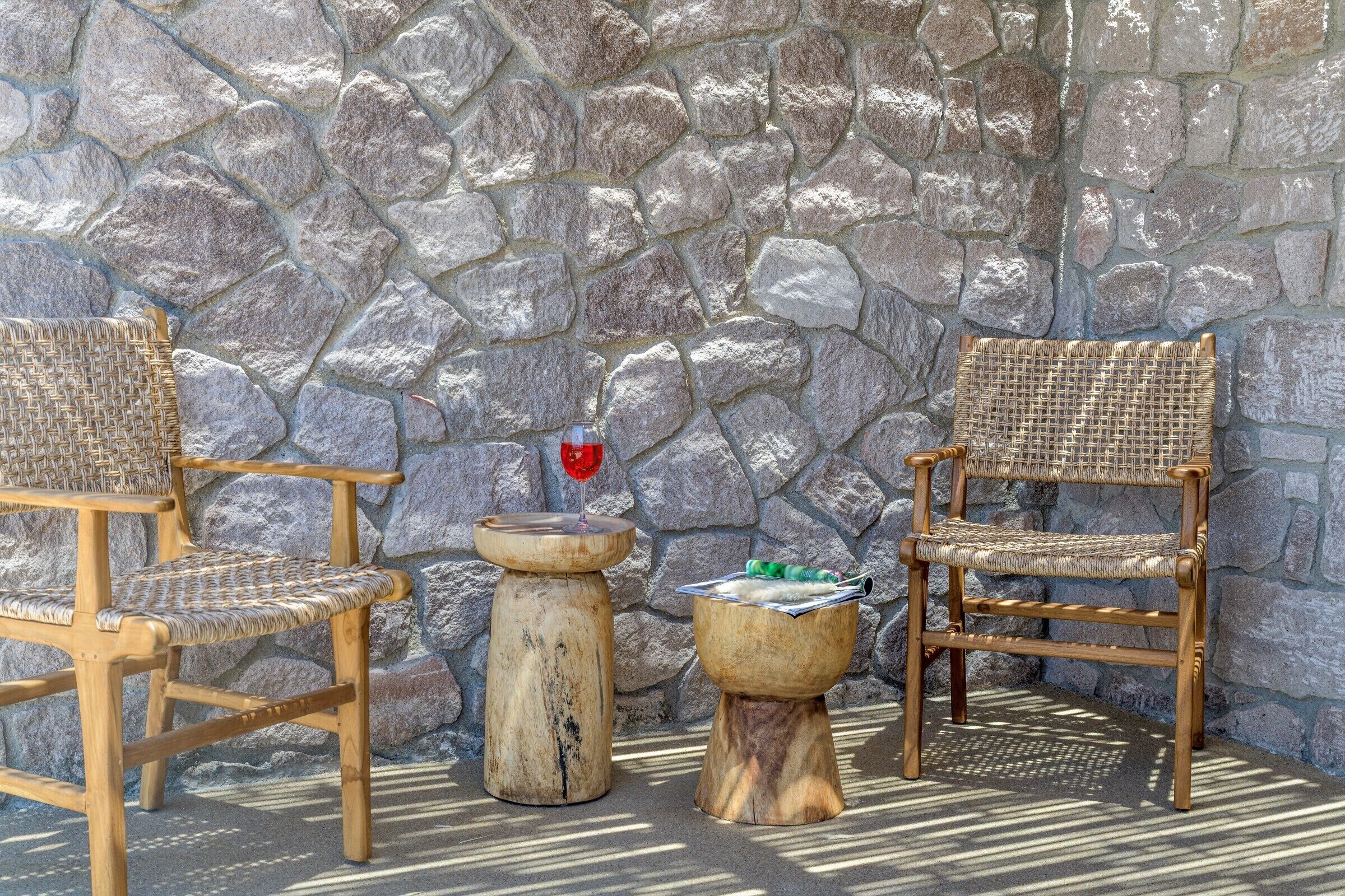Deux chaises en osier et une petite table avec une boisson, le tout placé devant un mur de pierre.