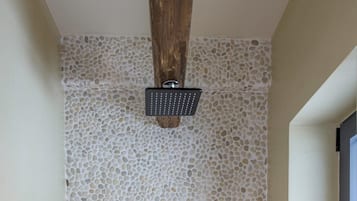 Ducha con pared de textura de guijarros, cabezal de ducha manual y un mando.