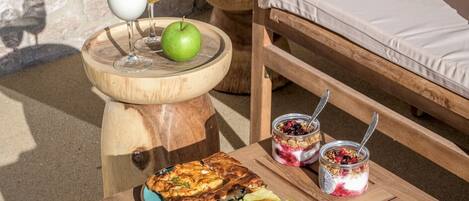 Une table en bois avec de la nourriture, une chaise et un mur de pierre en arrière-plan.