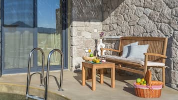 Un muro de piedra, un banco de madera, una cesta de mimbre y una zona junto a la piscina.