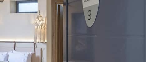 Ein modernes Hotelzimmer mit Bett, Nachttisch und einer Tür mit der Aufschrift 'PLATHIEN 9'.