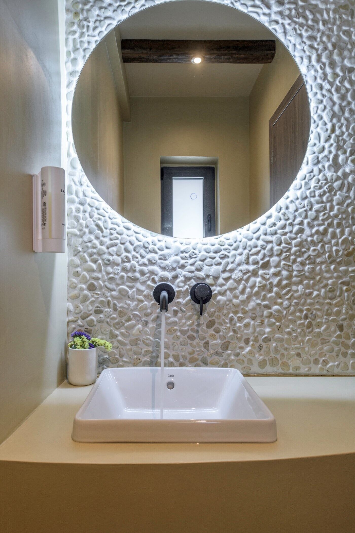 A bathroom with a round mirror, a rectangular sink, and a textured wall.