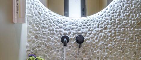 A bathroom with a round mirror, a rectangular sink, and a textured wall.