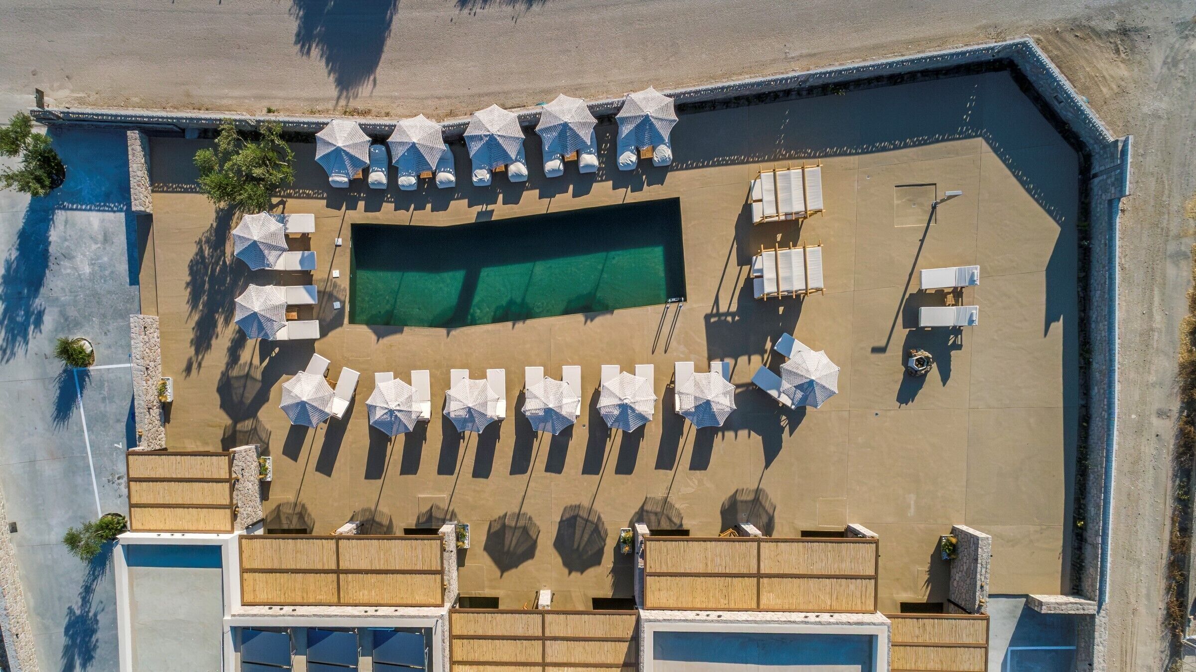 Vista aérea de un complejo turístico frente a la playa, con piscina, tumbonas y sombrillas.
