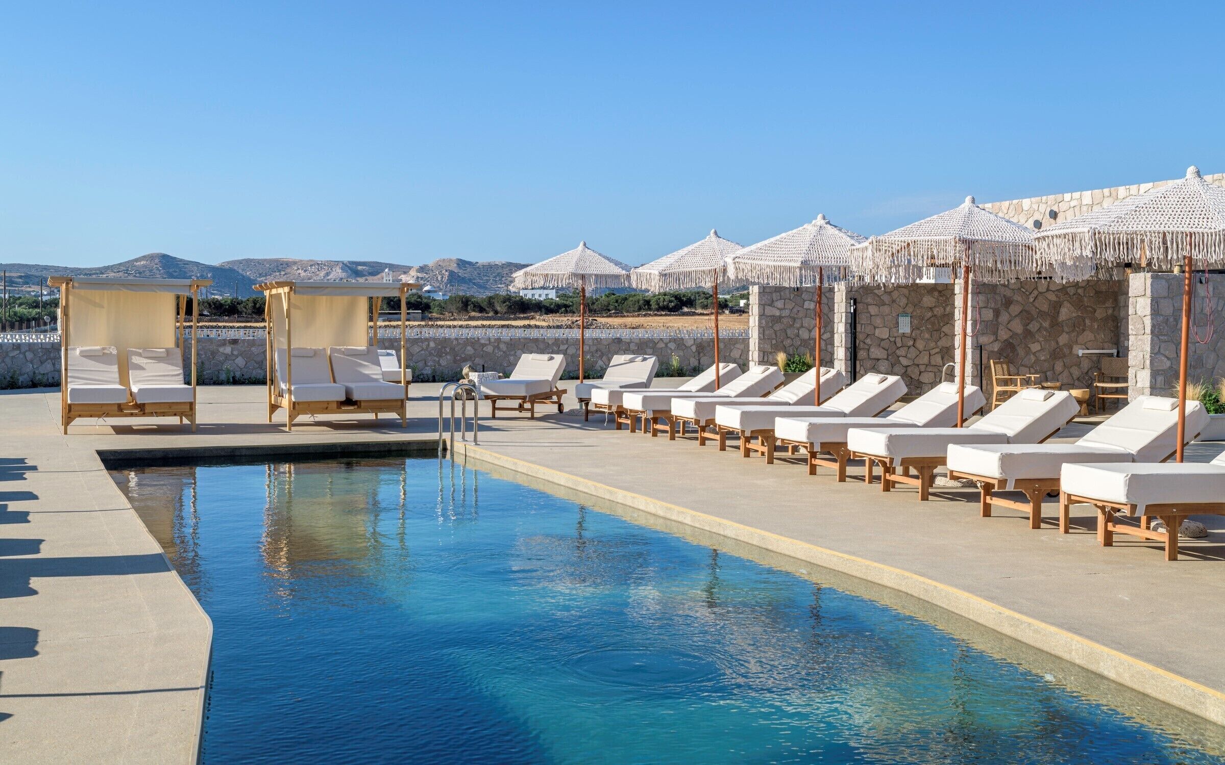 A poolside area with lounge chairs and a pool, surrounded by stone walls and umbrellas.