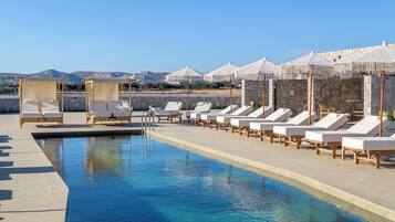 A poolside area with lounge chairs and a pool, surrounded by stone walls and umbrellas.