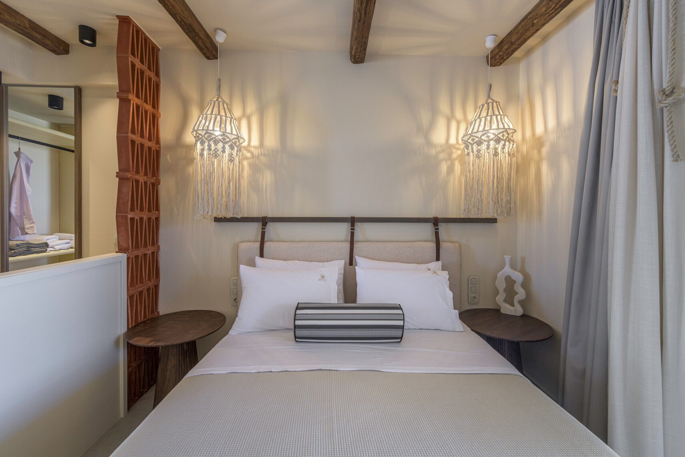 A neatly arranged bedroom with a bed, two bedside tables, a hanging light fixture, and a mirror.