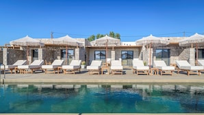 A poolside area with lounge chairs and umbrellas, stone walls, and large windows.
