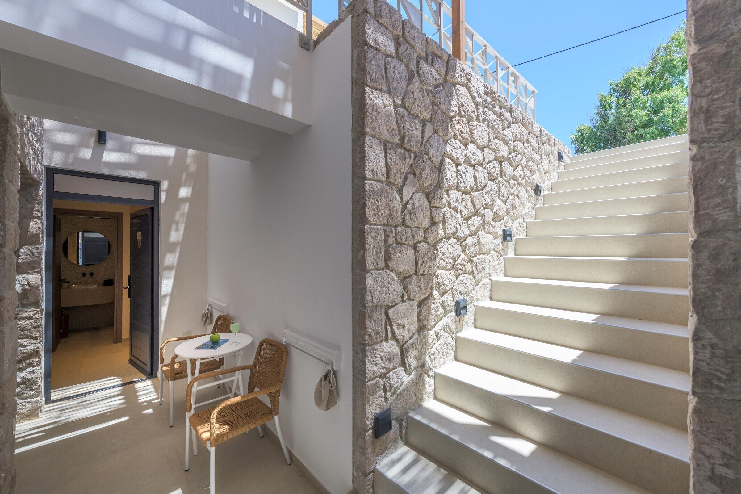 A stone staircase leading to a balcony, a small table with chairs, and a door to a room.