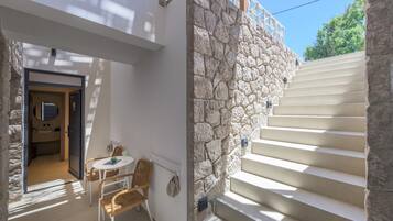 Una escalera de piedra que conduce a un balcón, una pequeña mesa con sillas y una puerta a una habitación.