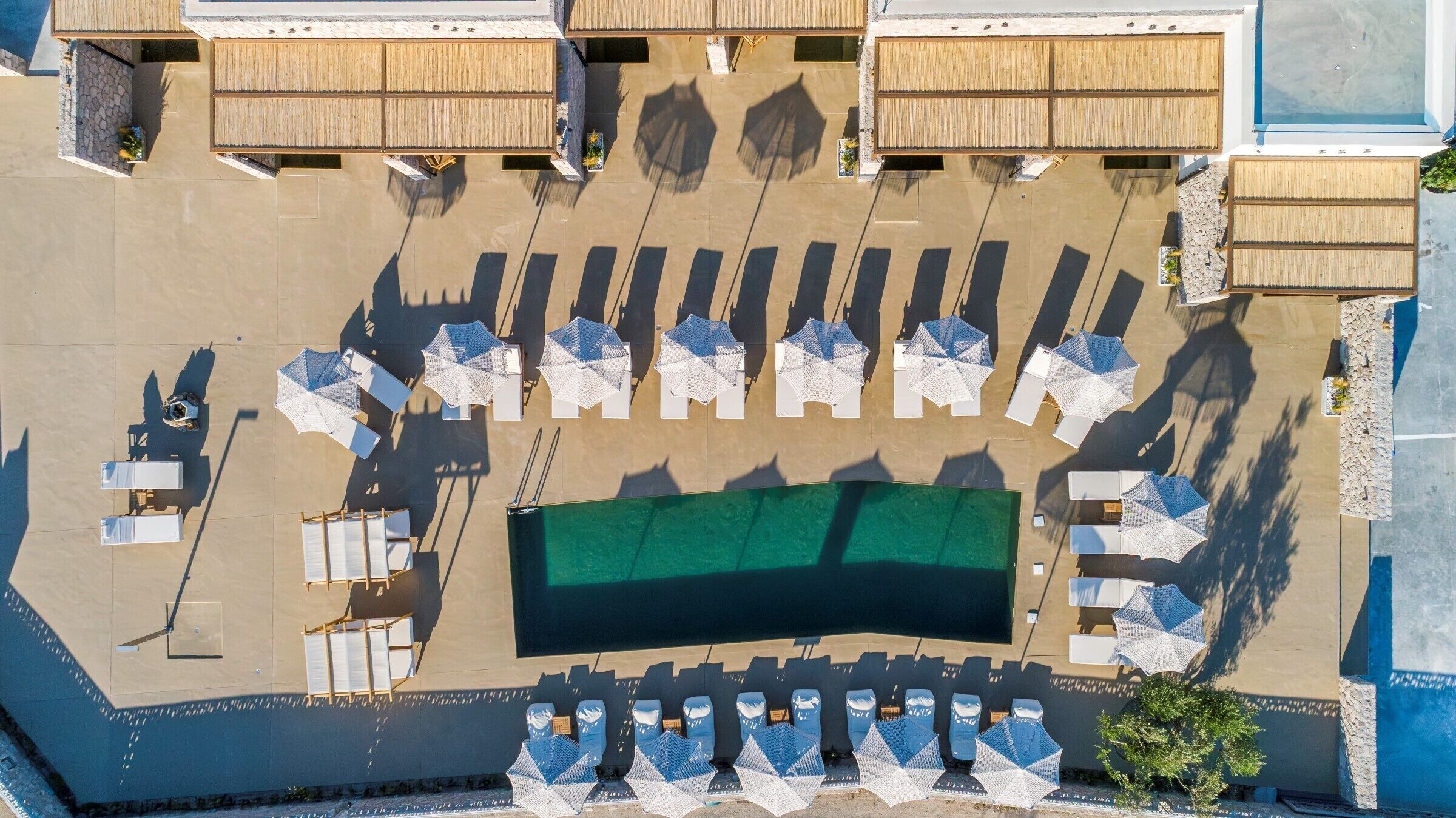 An aerial view of a hotel with a swimming pool, sun loungers, and umbrellas arranged around the pool area.