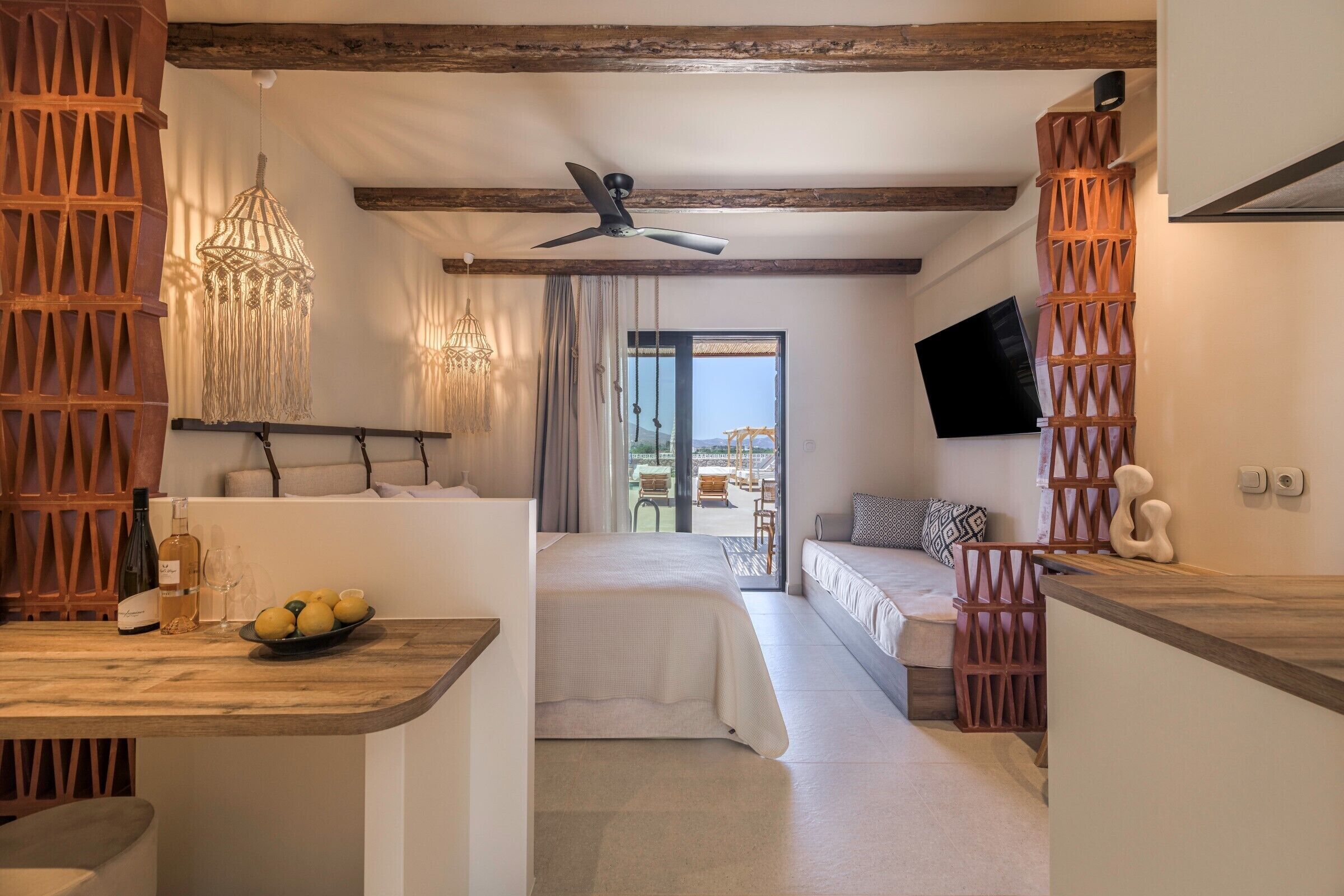 Habitación de hotel moderna con cama, zona de comedor, televisor y balcón con vistas.