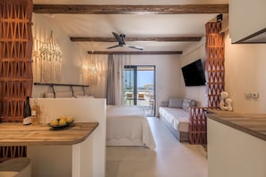 A modern hotel room with a bed, a dining area, a TV, and a balcony with a view. - Zefyria Luxury Suites (Milos)