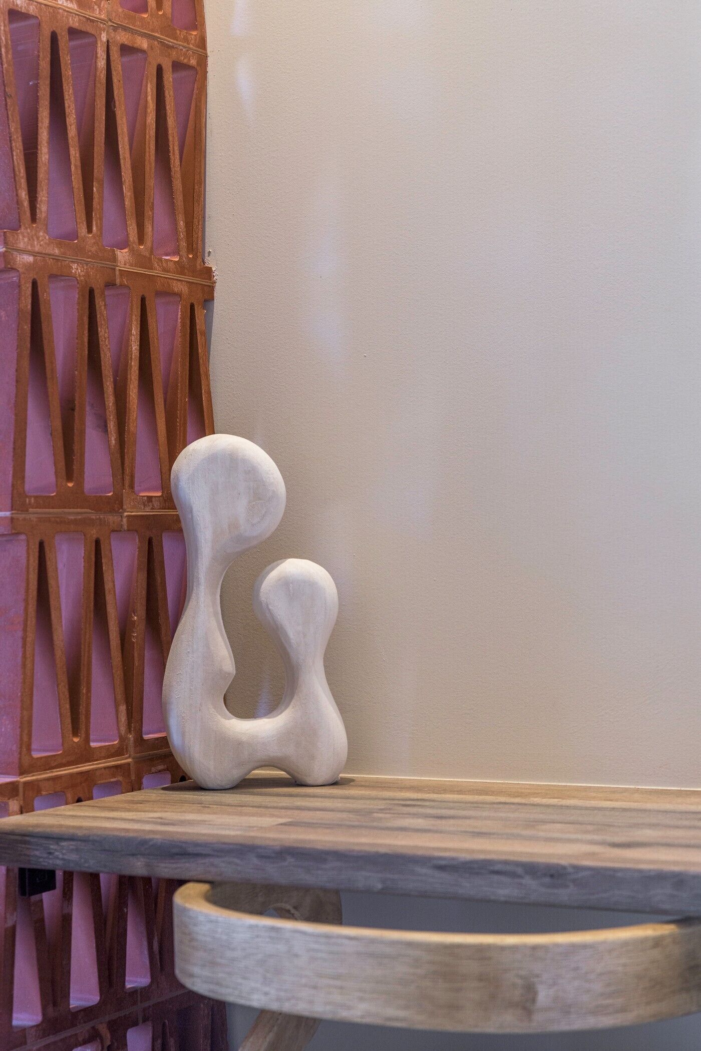 A wooden table with two white sculptures on it, a woven basket, and a plain wall.
