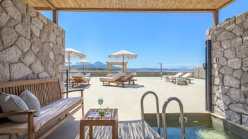 Zona de piscina con sillones reclinables, un banco de madera y una mesa con una bebida.