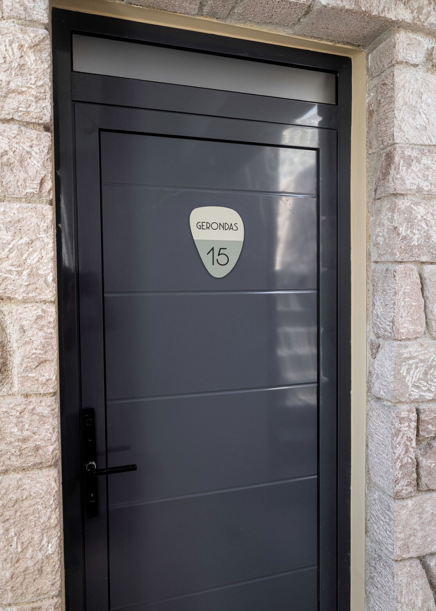 A black door with a stone wall, a doorbell, and a sign that reads 'Gerondas 15'.