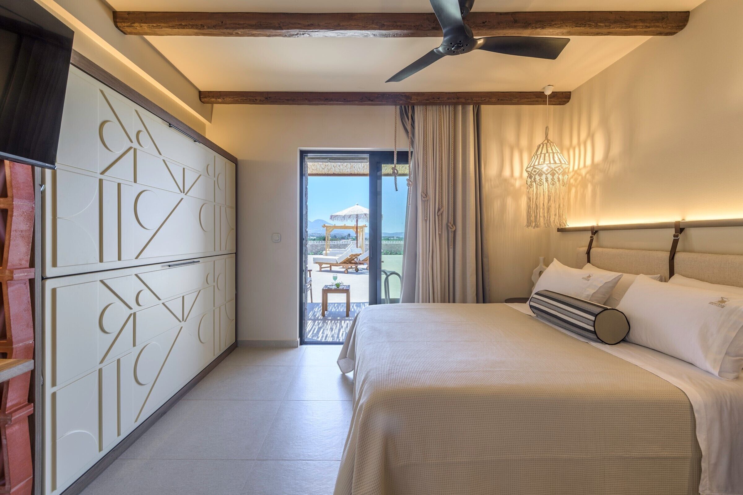 Une chambre à coucher avec un lit, un ventilateur de plafond, un lustre et une vue sur l’extérieur.