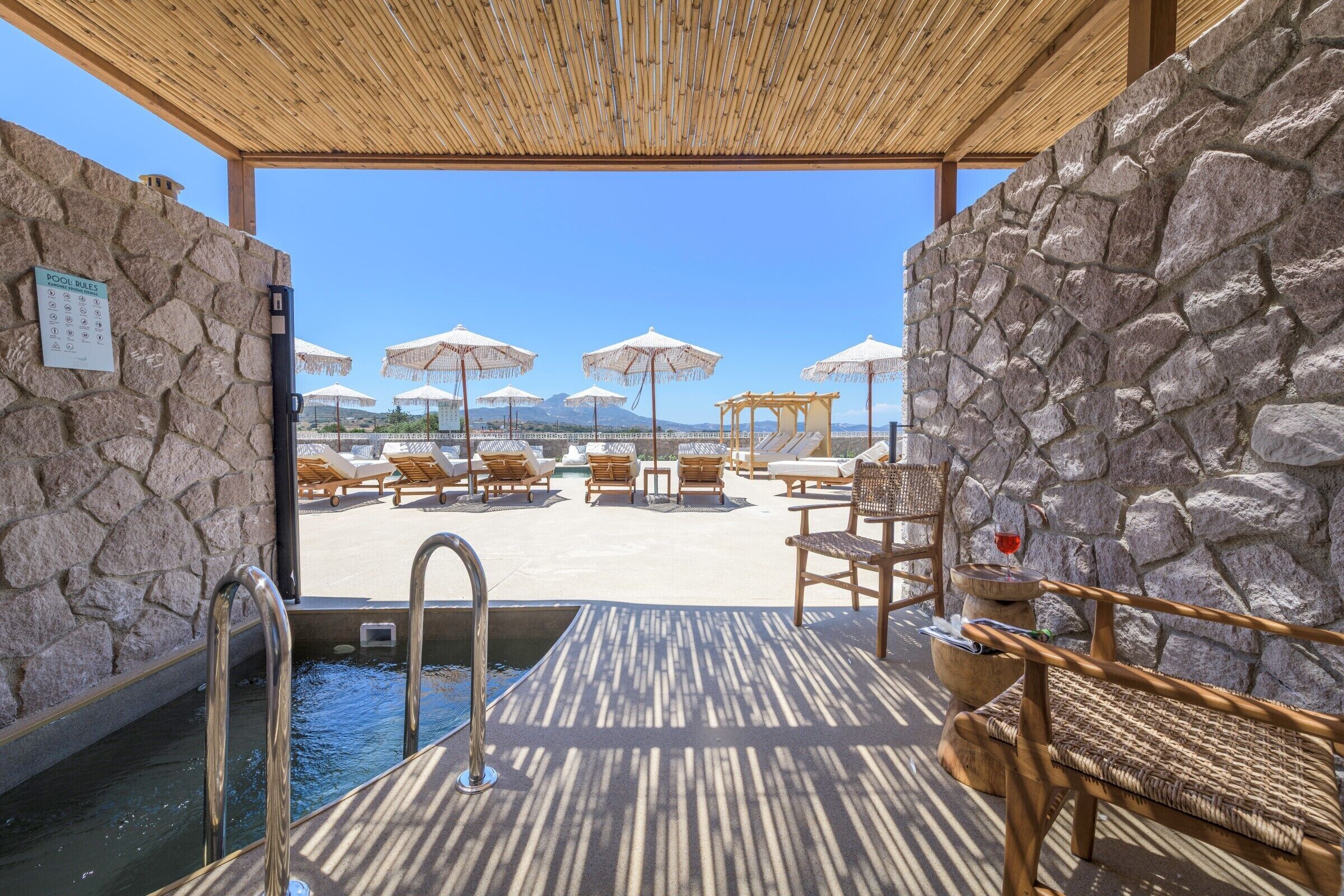 A pool area with stone walls, lounge chairs, umbrellas, and a wooden deck.