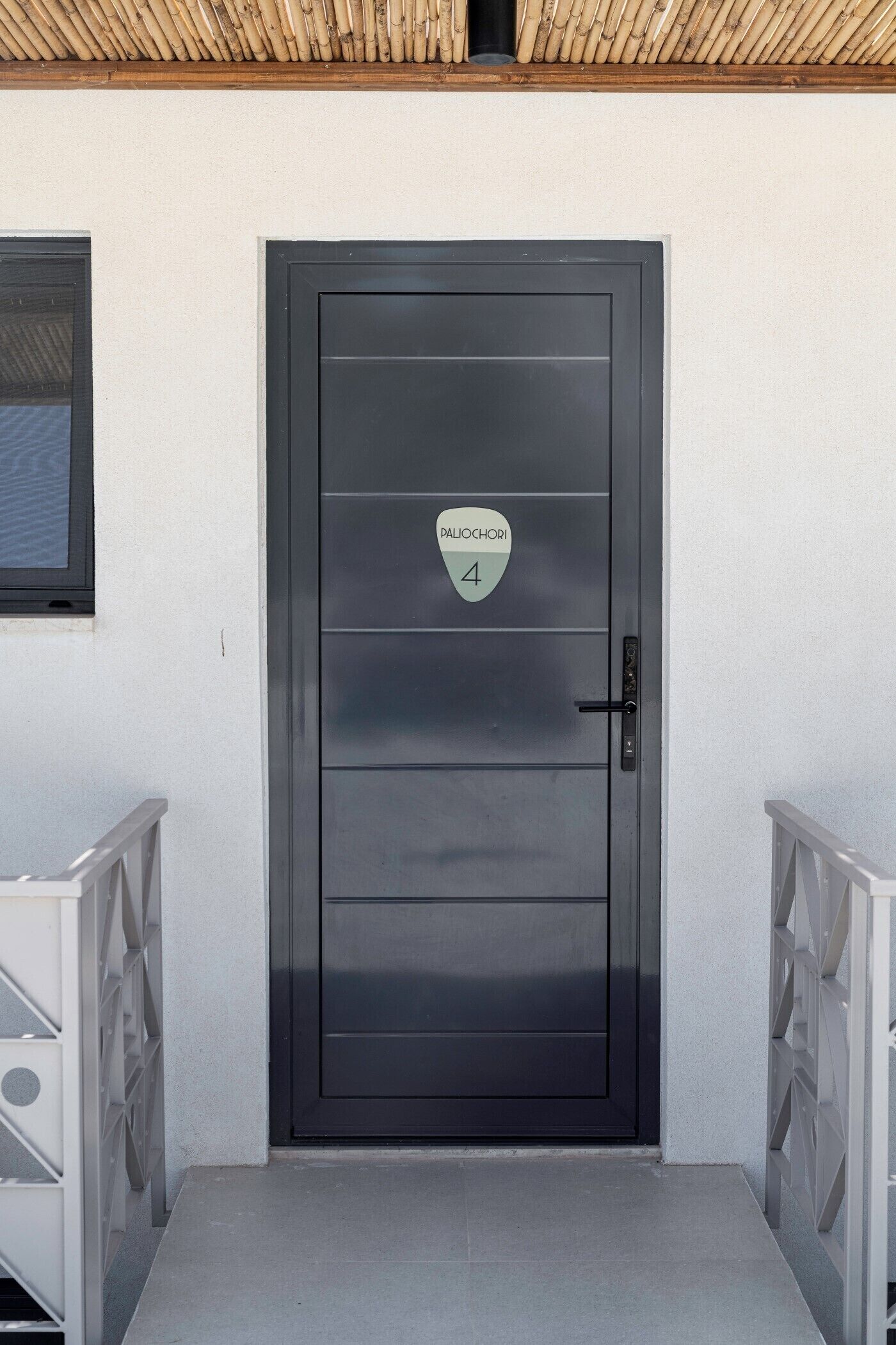 Una puerta negra moderna con un letrero que indica el número 4 de la habitación, un picaporte metálico y una pared blanca con una ventana a la izquierda.