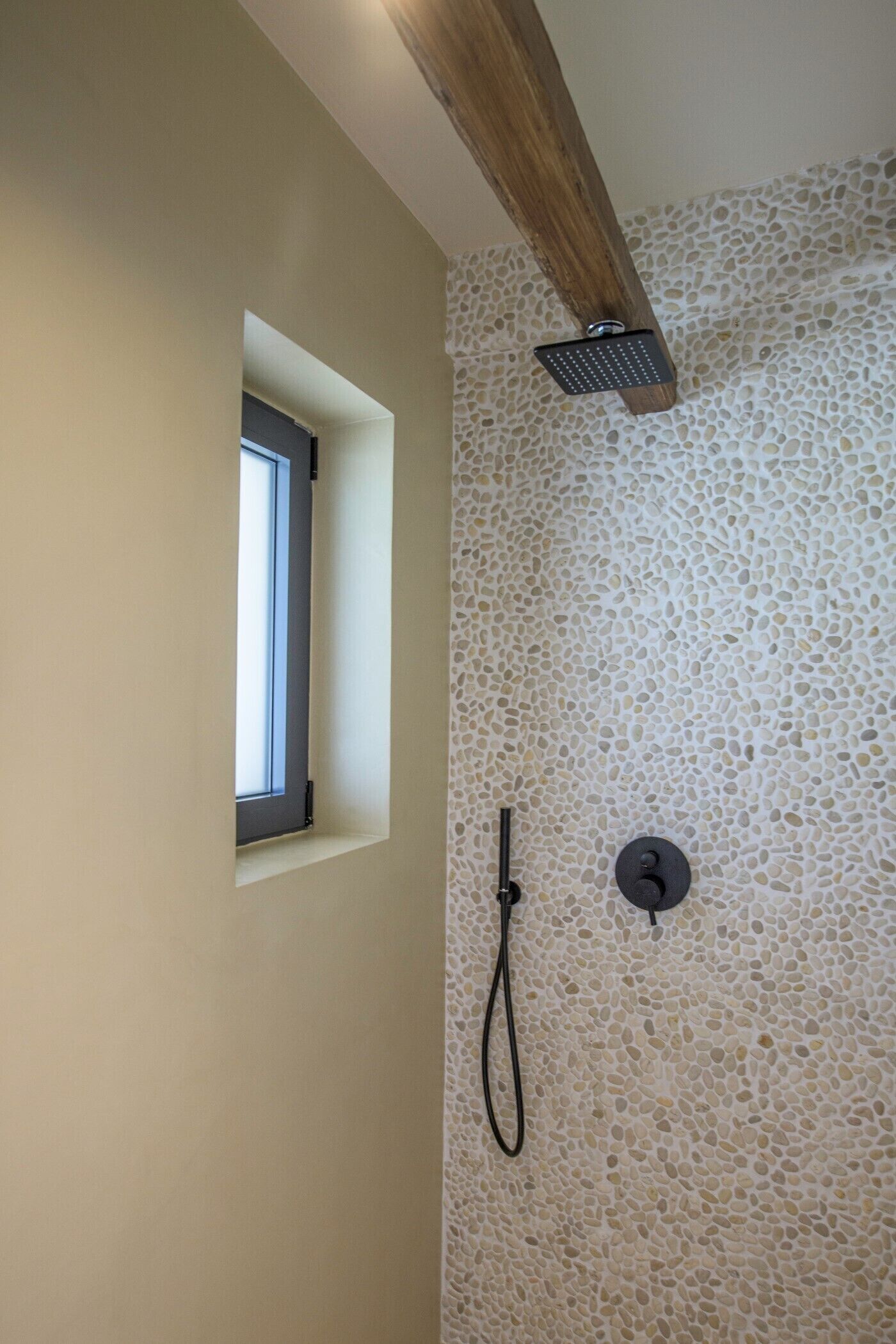 A shower with a stone wall, a window, and a wooden beam.