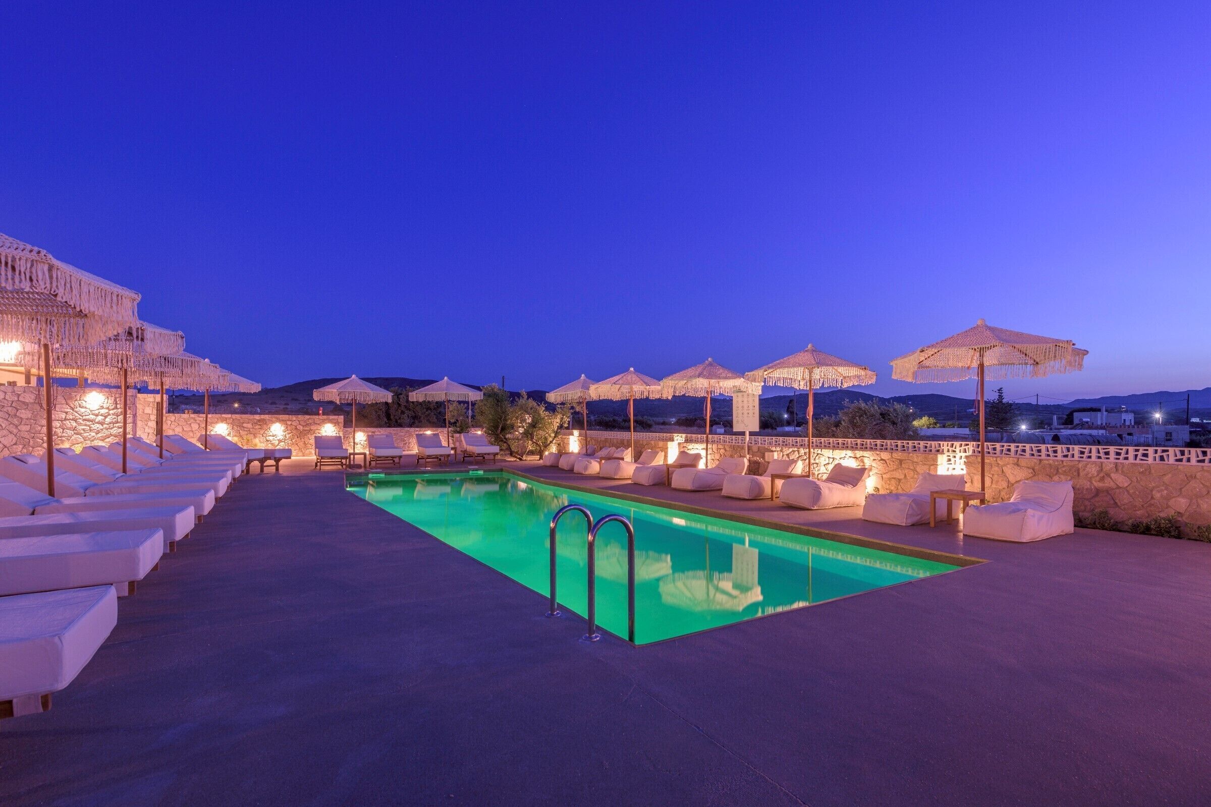 A rooftop pool area with lounge chairs and umbrellas, surrounded by stone walls and a clear view of the sky.