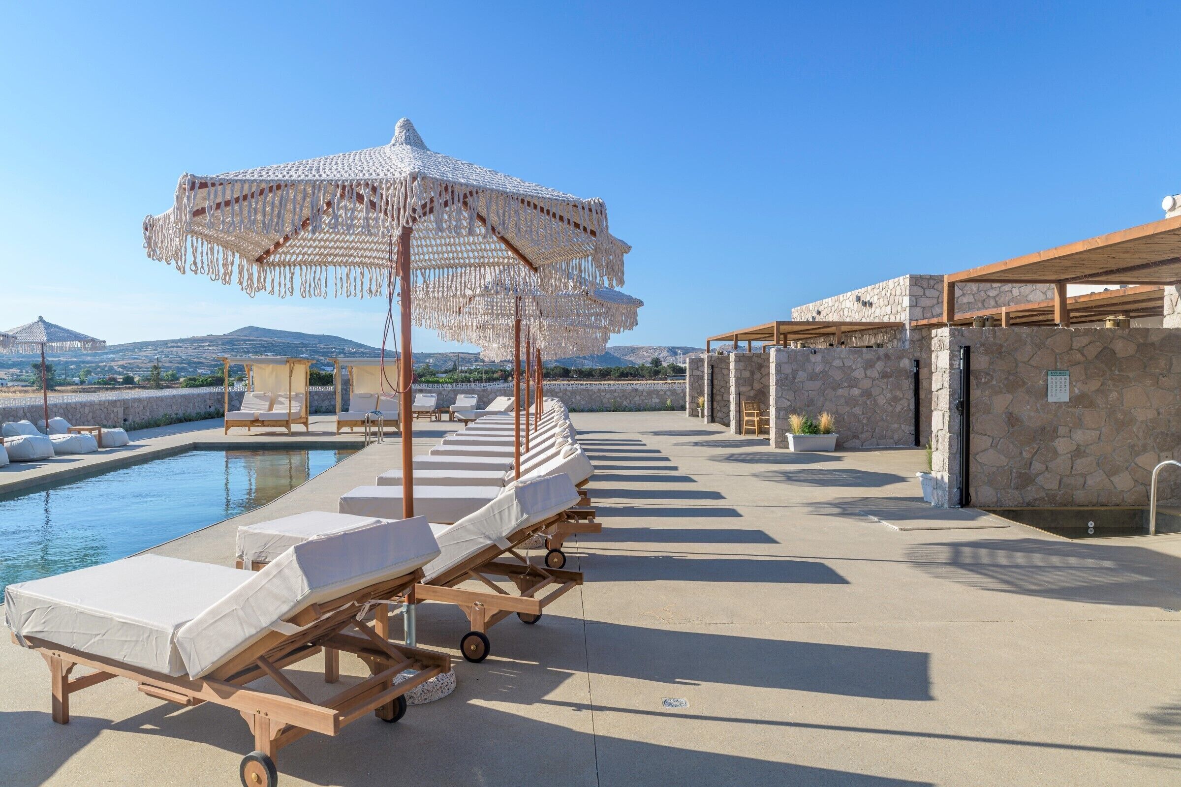 A poolside area with lounge chairs, a canopy, and a stone wall.