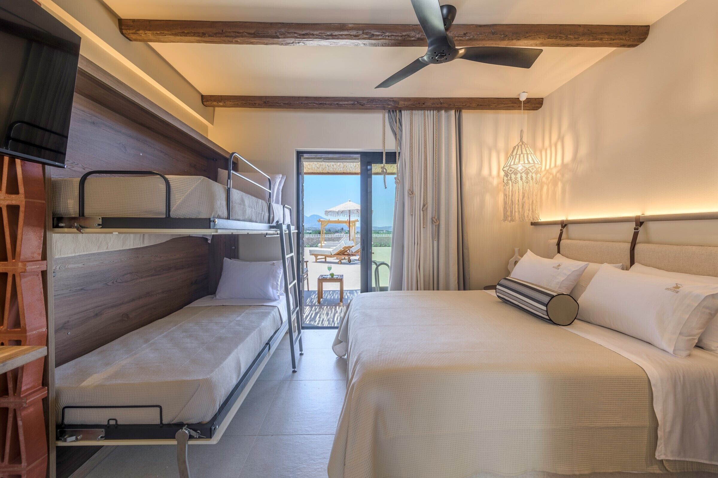 Camera d'albergo con letto a castello, un letto singolo, ventilatore a soffitto, televisione e vista sull'esterno.