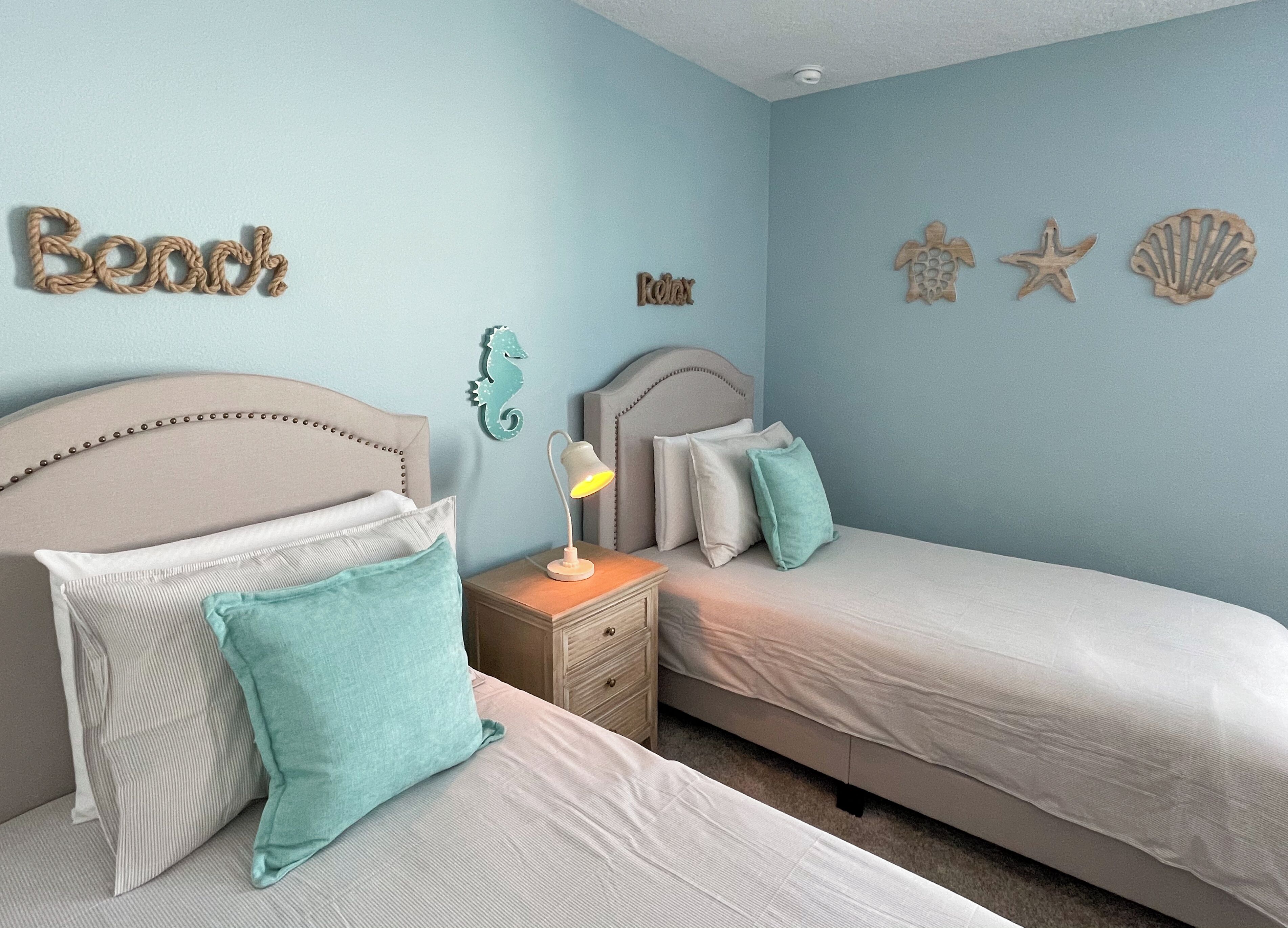 Une chambre avec deux lits, une table de chevet, une lampe et des éléments de décoration murale, notamment un hippocampe, des étoiles de mer et des coquillages.