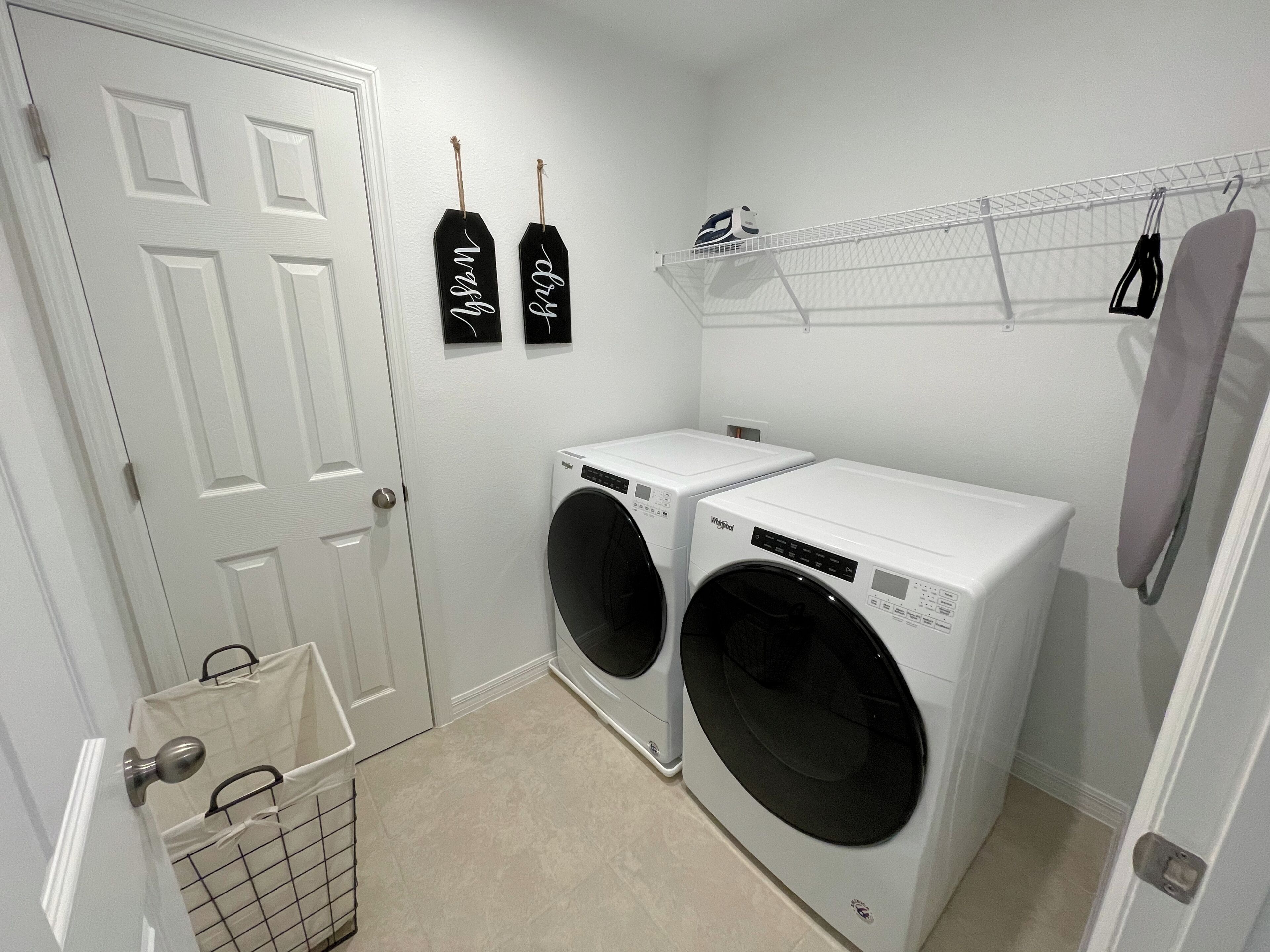 A laundry room with two front-loading washers, a drying rack, and a basket.