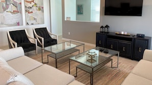 A modern living room with a sofa, two armchairs, a glass coffee table, a TV, and artwork on the walls. - 8957-HiltonRidge (Kissimmee)