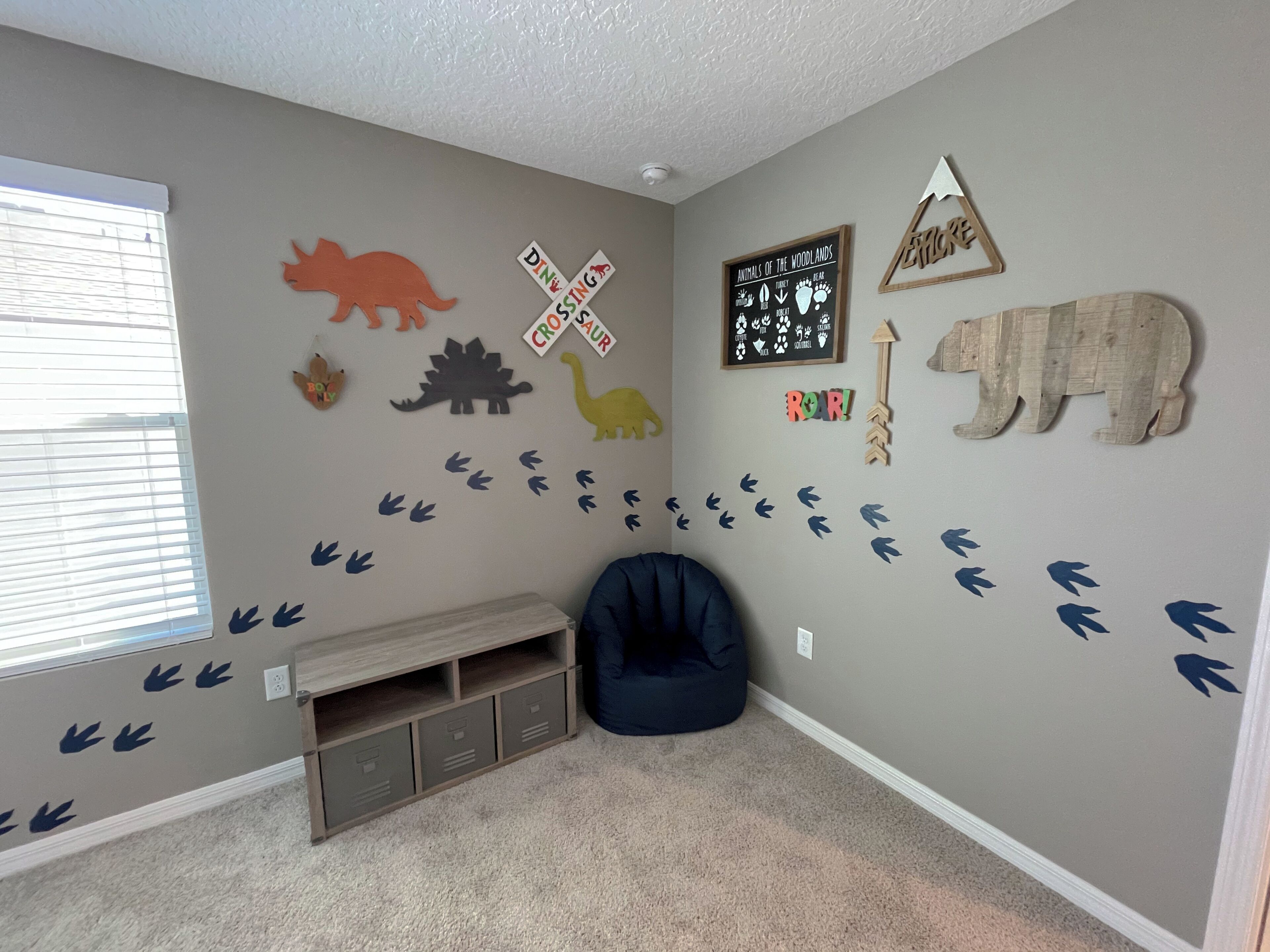 A room with a window, a blue bean bag chair, a shelf, and wall decorations including animal silhouettes and a dinosaur.