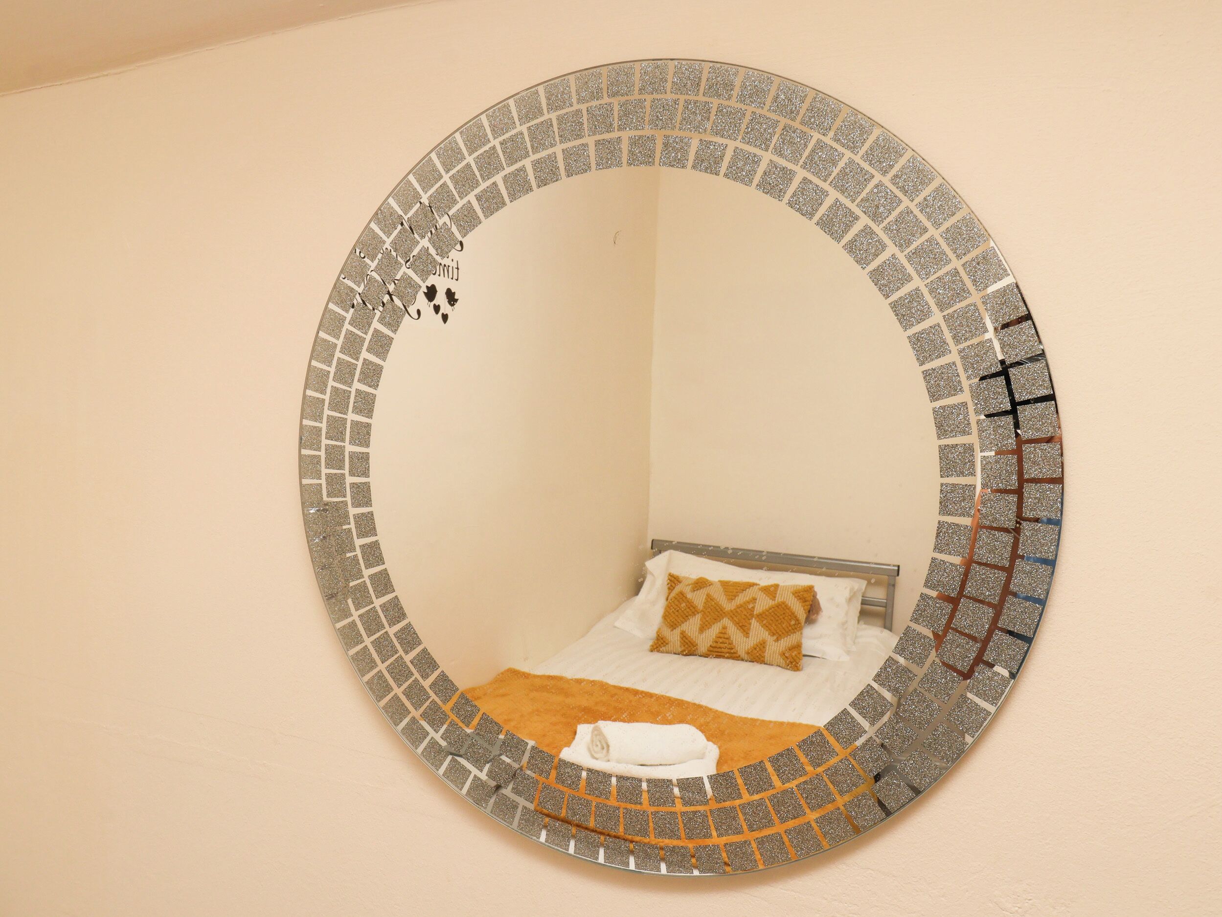 Ein runder Spiegel mit Mosaikbordüre an einer Wand.